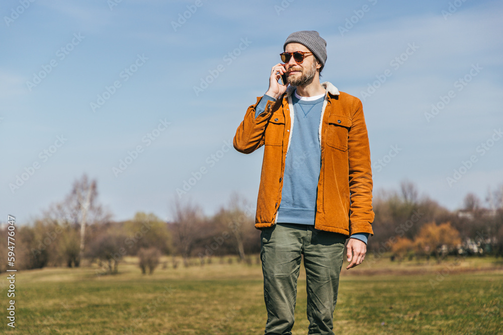a man with a beard in a gray cap, velvet jacket, holds a smartphone in his hands and speaks on the phone a man with a beard in a gray cap, velvet jacket, holds a smartphone in his hands and speaks on the phone