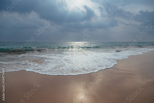 Fototapeta Naklejka Na Ścianę i Meble -  A gorgeous view of a sandy ocean beach with turquoise waves under a dramatic cloudy sky with sunlight through it.