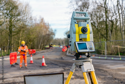 Site engineer operating his instrument during roadworks. Builder using total positioning station tachymeter on construction site for new road setting out