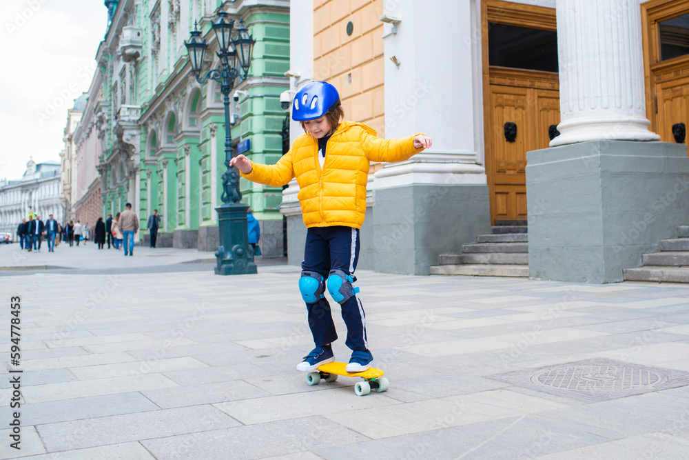 a boy in a protective helmet rides a yellow city curezer, a plastic skateboard in the spring through the urban streets of the old city a boy in a protective helmet rides a yellow city curezer, a plastic skateboard in the spring through the urban streets of the old city