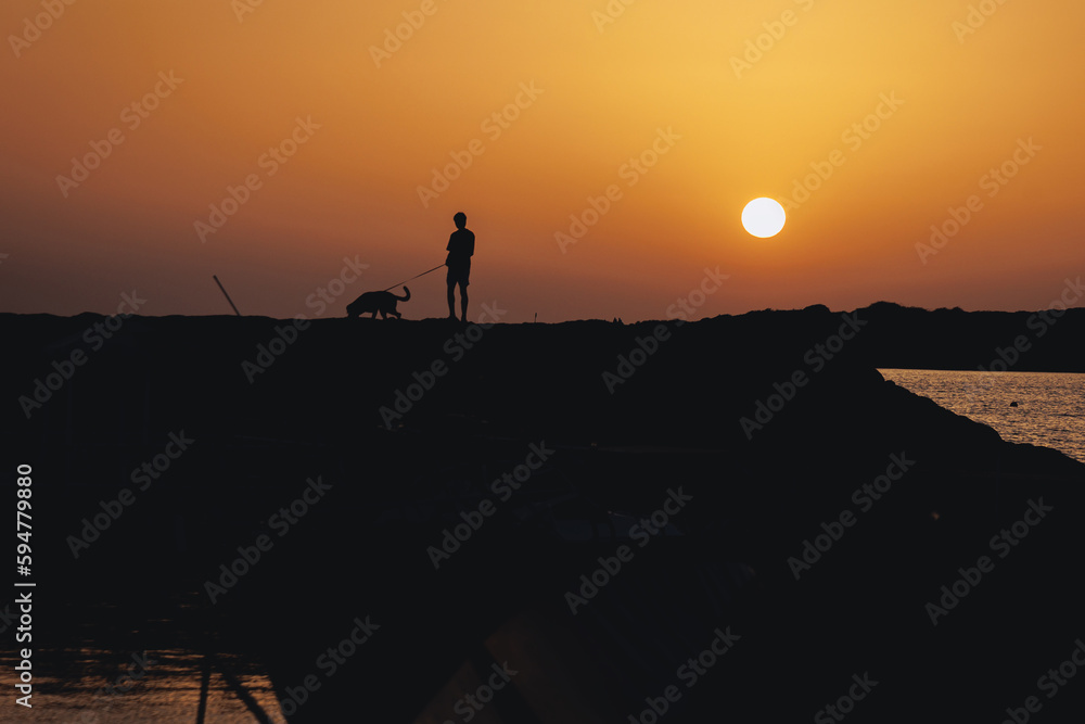 Man walks with a dog during sunset in Coral Bay resort, part of Pegeia city, Cyprus