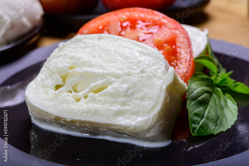Sliced white ball of Italian soft cheese Mozzarella di Bufala Campana served with fresh green basil and red tomato