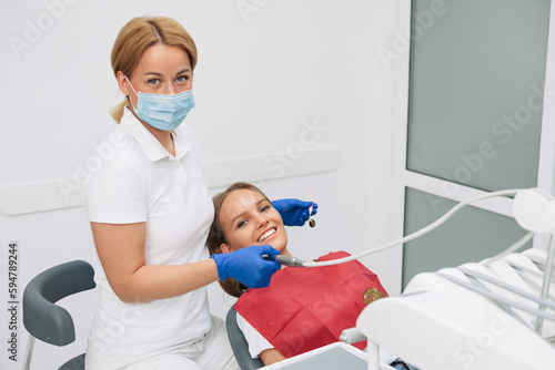A woman receives dental treatment. The doctor and the patient are looking at the camera happily
