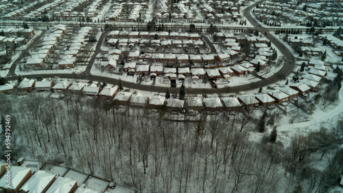 An aerial drone shot of a creek running through a forest with houses on the side during winter
