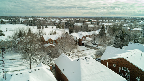An aerial drone shot of houses and a park covered in snow in the winter