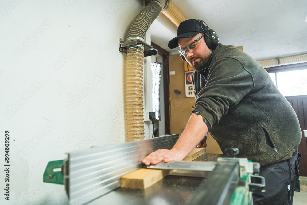 A woodworking machine used to produce a flat surface along a board's length. Focused woodworker in protective gear working. High quality photo A woodworking machine used to produce a flat surface along a board's length. Focused woodworker in protective gear working. High quality photo