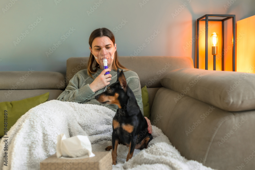 A 40-year-old woman inhales with a nebulizer while sitting on the couch Treatment of the respiratory tract, treatment of allergies with the help of inhalation of medicines