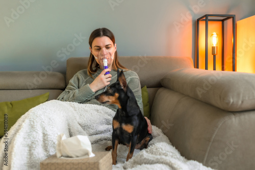 Obraz na płótnie A 40-year-old woman inhales with a nebulizer while sitting on the couch Treatment of the respiratory tract, treatment of allergies with the help of inhalation of medicines w salonie