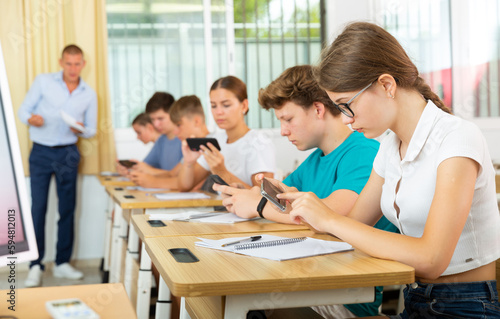 Teenager students sitting in class room and using their smartphones.