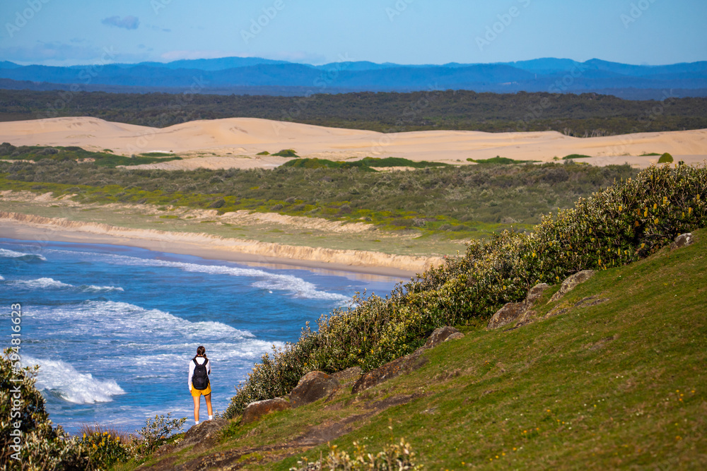 beautiful backpacker girl enjoying spectacular view of new south wales coast in hat head national park, australia; sand dunes and long beach on the shore of pacific during sunrise