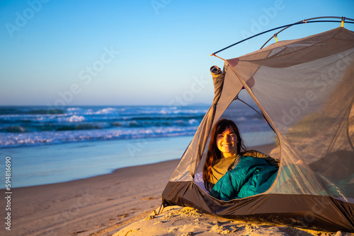 A beautiful girl admires a wonderful sunrise on the beach from her tent. Camping on the beach in Australia  Hat Head National Park  NSW