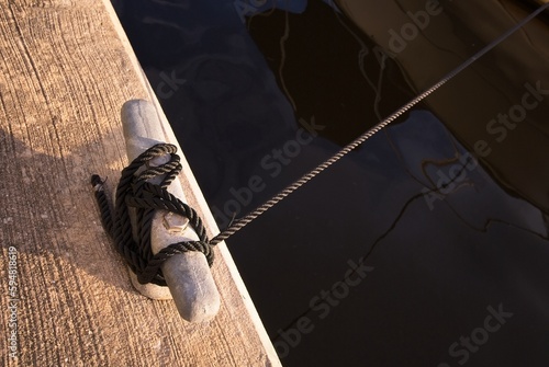 Fotografie Braided rope hitched to cleat on dock tied to distant boat