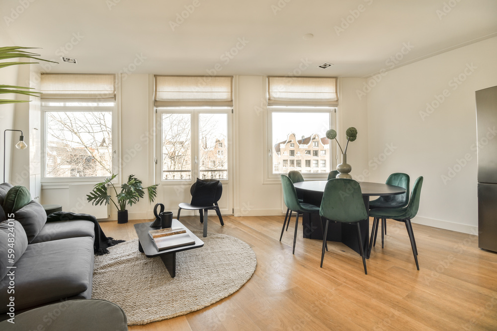 Fototapeta premium a living room with wood flooring and white walls, there is a black couch in front of the window