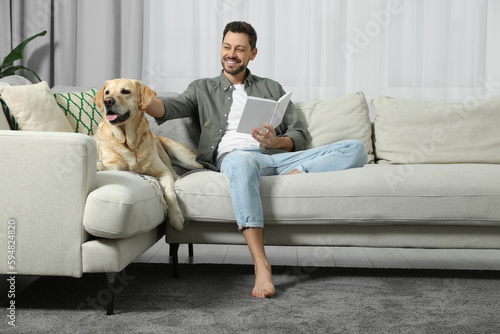 Man reading book on sofa near his cute Labrador Retriever at home