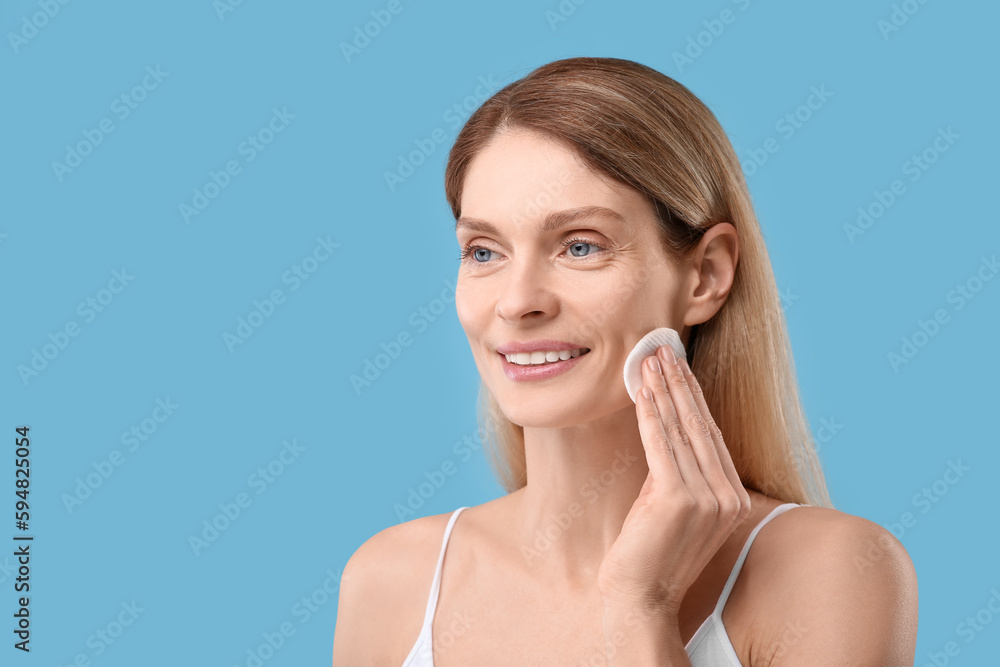 Beautiful woman removing makeup with cotton pad on light blue background, space for text Beautiful woman removing makeup with cotton pad on light blue background, space for text