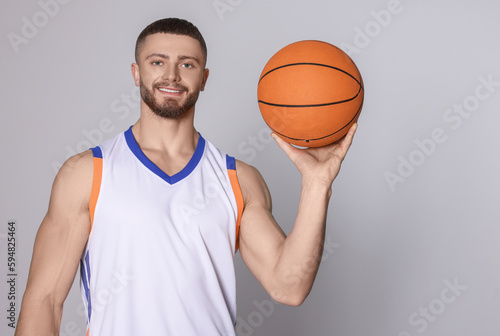 Athletic young man with basketball ball on light grey background. Space for text
