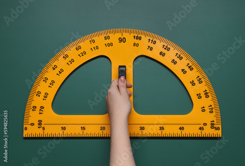 Woman holding protractor with measuring length and degrees markings near green board, closeup