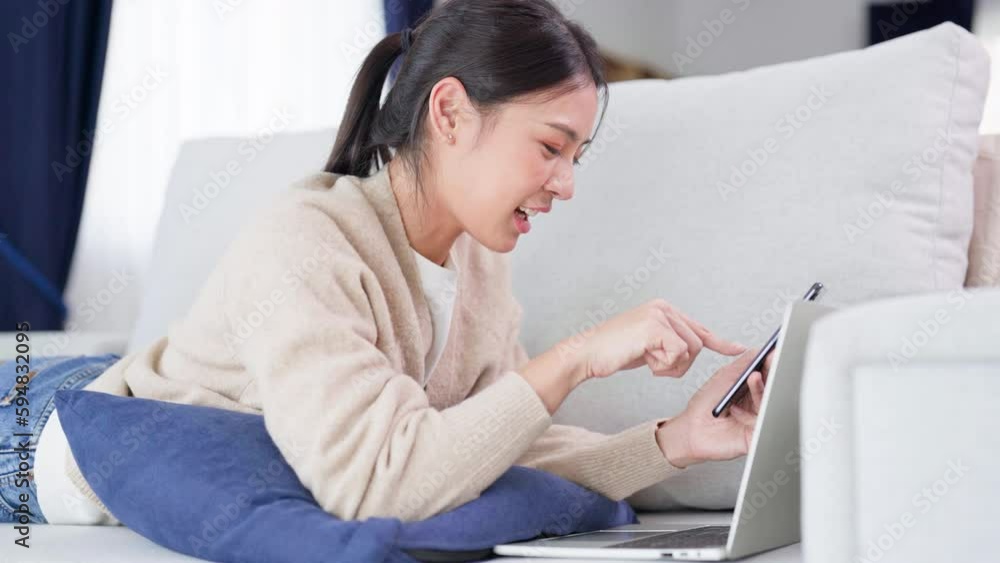 Happy young asian woman relaxing at home. Female smile lying on sofa and holding mobile smartphone. Girl using video call to friend Happy young asian woman relaxing at home. Female smile lying on sofa and holding mobile smartphone. Girl using video call to friend