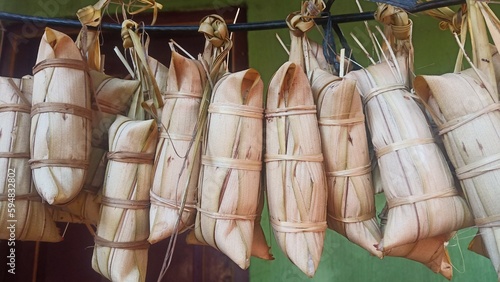 lepet rice cake covered with young coconut leaf and boiled 24 hours on traditional stove hanging in a rope photo