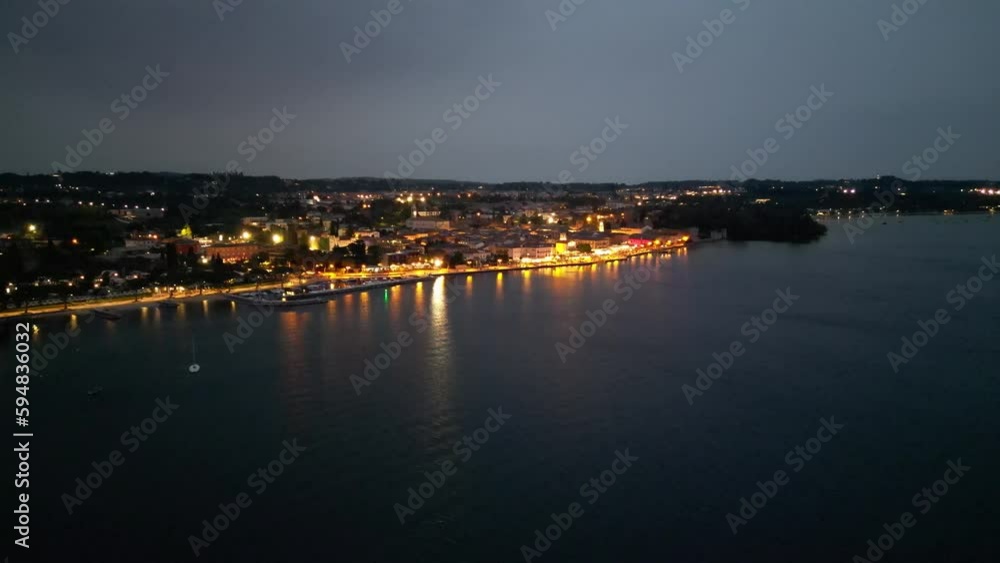 Stunning City Lights Of Lazise By The Shore Of Lake Garda At Night In Verona, Italy. aerial pull-back Stunning City Lights Of Lazise By The Shore Of Lake Garda At Night In Verona, Italy. aerial pull-back