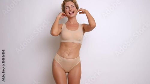 A beautiful young woman with curly hair moves sexually against the backdrop in the studio, dressed in a comfortable lingerie beige top and panties, underclothing fashion concept, copy space, high