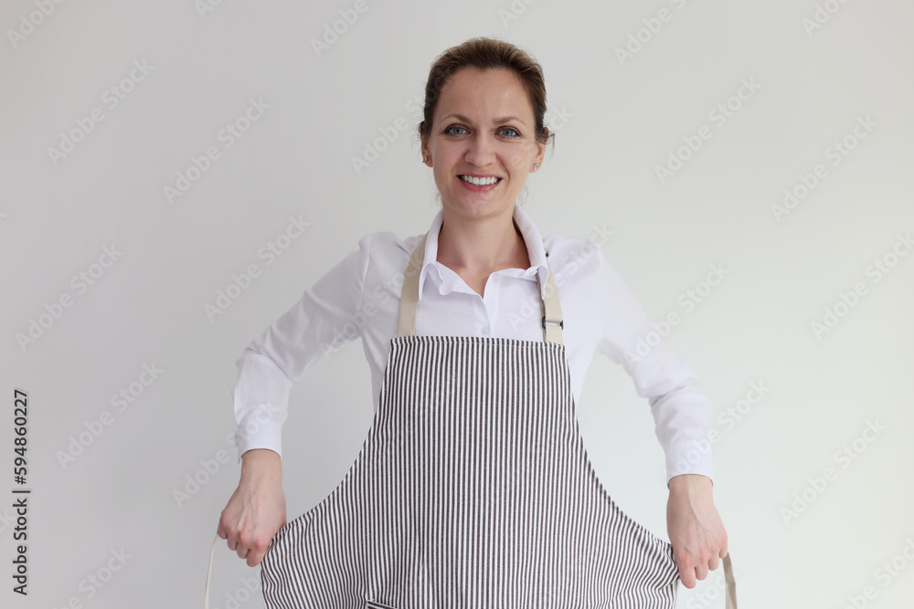 Young woman puts on striped apron smiling with satisfaction Young woman puts on striped apron smiling with satisfaction