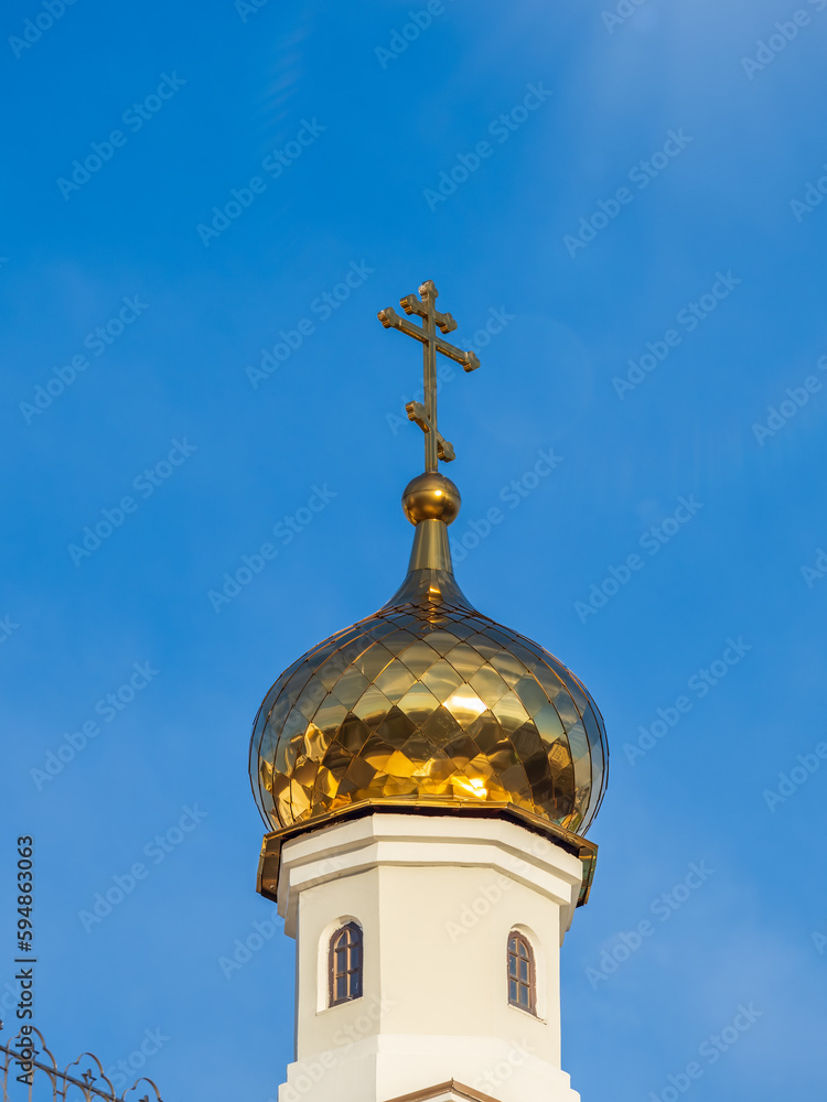 Gilded dome with a cross of an Orthodox church against a blue clear sky