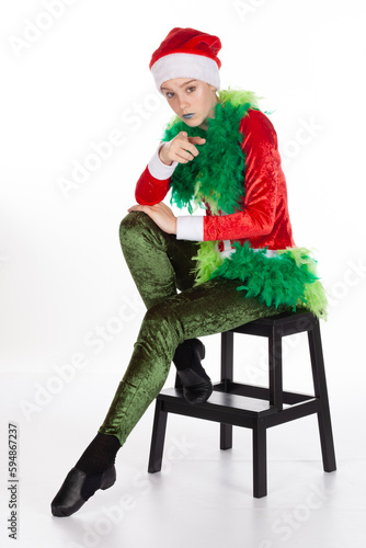 Naughty you expression by sitting young teen girl grinch pointing, grumpy greedy wearing red santa clause hat, isolated on white background. Negative human emotion facial expression
