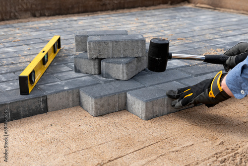 Construction worker laying cement pavement on a walkway with gloves and rubber hammer. House improvement.