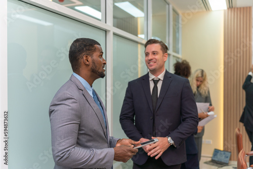 Two businessmen having a discussion and chit chat about latest market trend while waiting the meeting to start. Businessman talking.