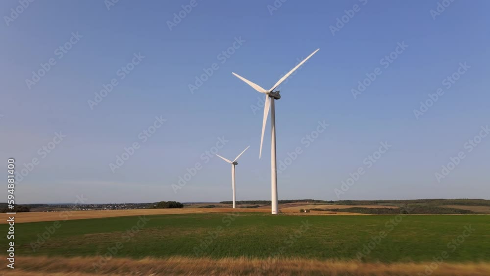 Drone flying towards two isolated windmills spinning under blue sky. Hope for future Drone flying towards two isolated windmills spinning under blue sky. Hope for future