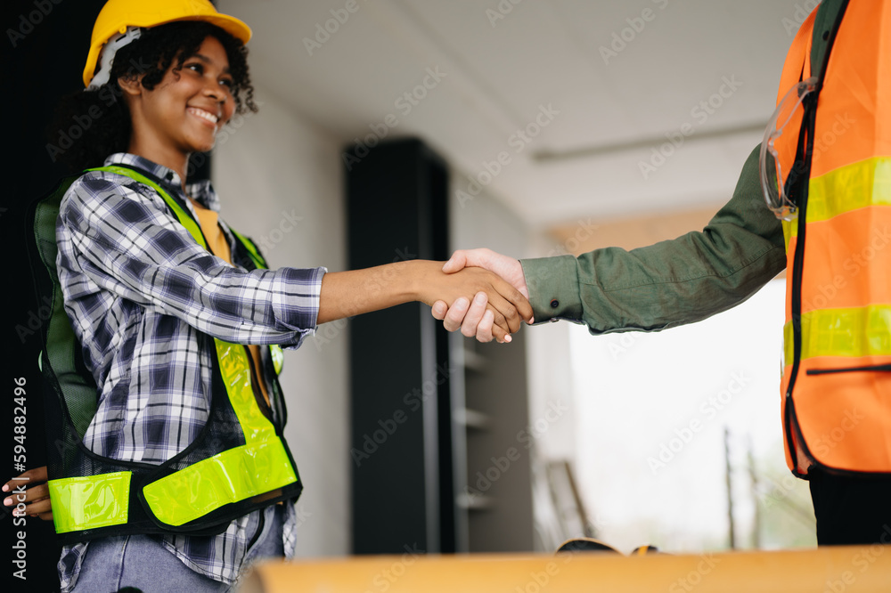 Construction team shake hands greeting start new project plan behind yellow helmet on desk in office center to consults about their building project.. Construction team shake hands greeting start new project plan behind yellow helmet on desk in office center to consults about their building project..