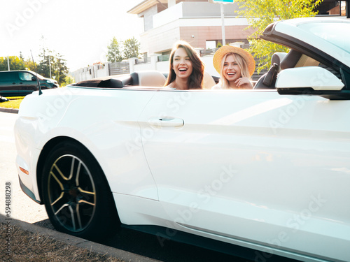 Portrait of two young beautiful and smiling hipster female in convertible car. Sexy carefree women driving. Positive models riding and having fun outdoors. Enjoying summer days. Cheerful and happy © halayalex
