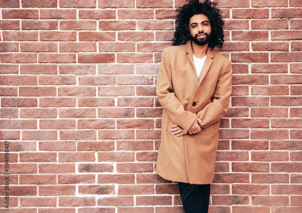 Handsome confident hipster model. Unshaven Arabian man dressed in brown coat clothes. Fashion male with long curly hairstyle posing in the street near brick wall. Cheerful and happy Handsome confident hipster model. Unshaven Arabian man dressed in brown coat clothes. Fashion male with long curly hairstyle posing in the street near brick wall. Cheerful and happy