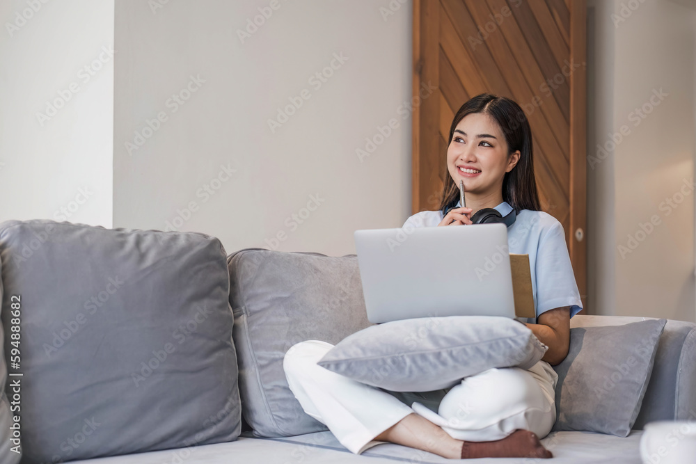 young student wearing headphones studies online,conversation via video call,distance learning on the sofa in the house young student wearing headphones studies online,conversation via video call,distance learning on the sofa in the house