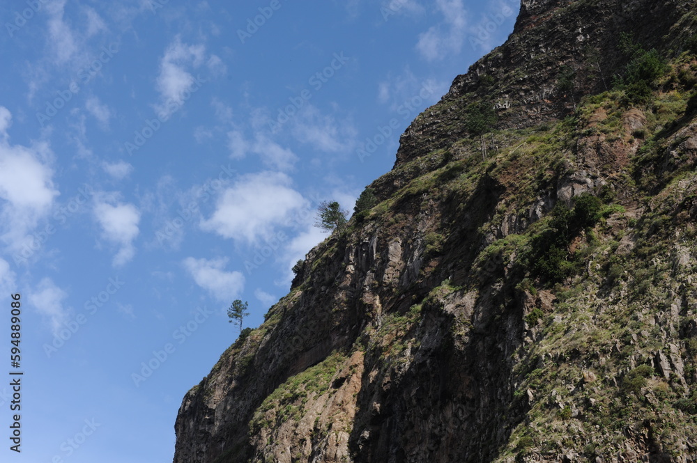 Steep mountain rock slope landscape with green trees an the top peak and blue sky and blue sky Steep mountain rock slope landscape with green trees an the top peak and blue sky and blue sky