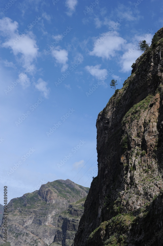 Steep mountain rock slope landscape with green trees an the top peak and blue sky and blue sky Steep mountain rock slope landscape with green trees an the top peak and blue sky and blue sky