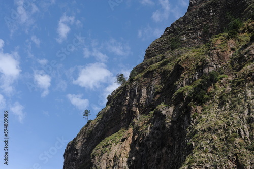 Steep mountain rock slope landscape with green trees an the top peak and blue sky and blue sky