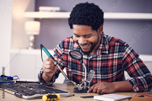 Black man, technician and fixing computer circuit board in hardware, soldering iron tools or tech repair. Maintenance, magnifying glass or electrical fix with happy male working on device motherboard photo