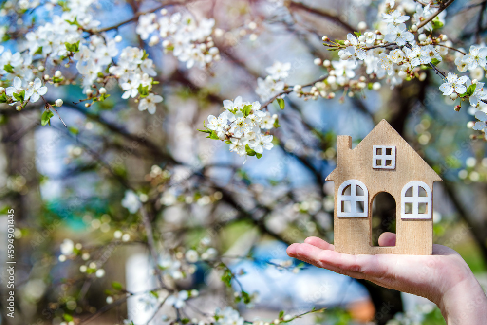 The girl holds the house symbol against the background of blossoming cherry
