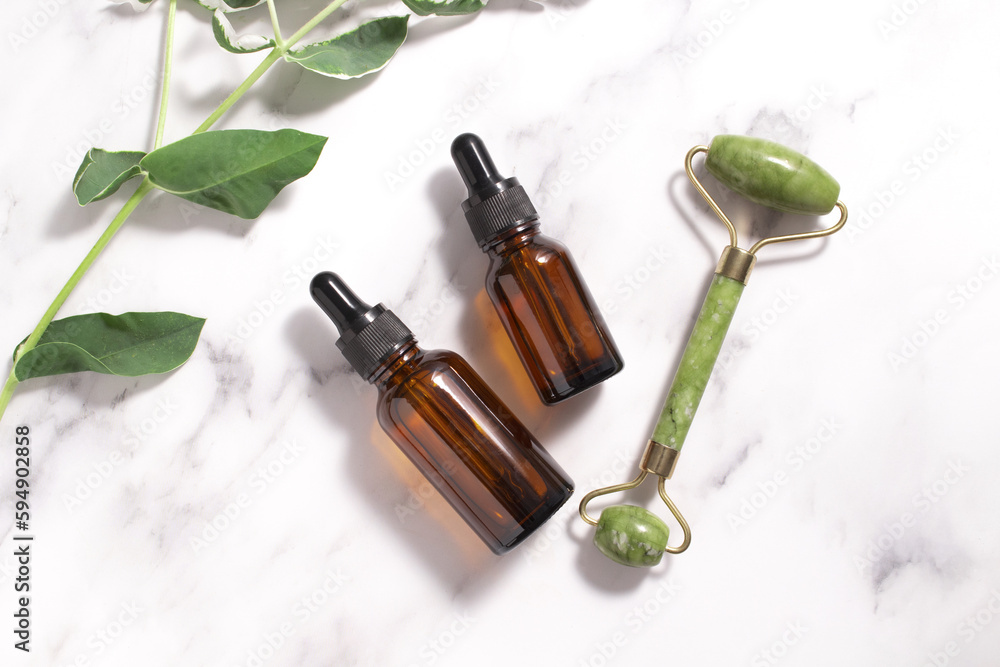 Unbranded serum bottle, face roller with leaves on marble background. Jade face roller for facial massage therapy. Anti age, lifting and toning treatment Unbranded serum bottle, face roller with leaves on marble background. Jade face roller for facial massage therapy. Anti age, lifting and toning treatment