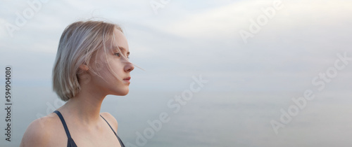 Portrait of blonde woman standing on the background of blue sea and cloudy sky