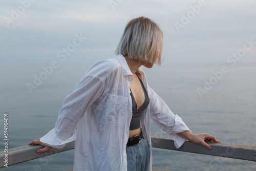 Portrait of blonde woman in white shirt and tank top looking backwards on the background of sea, cloudy sky