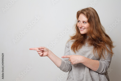 Young smiling woman pointing finger aside on white studio wall background