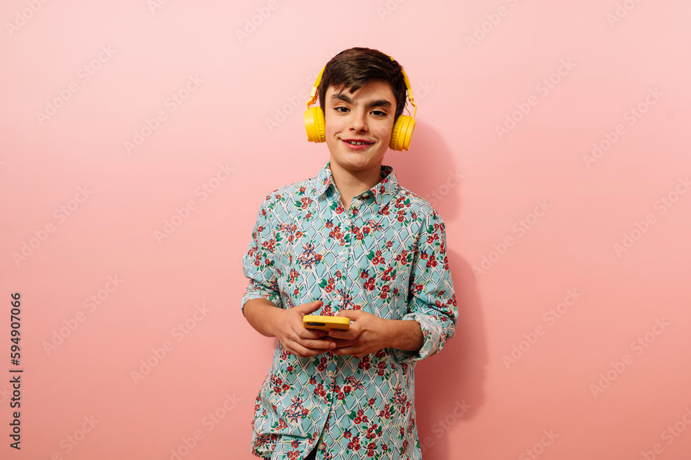 Young guy using smartphone and yellow headphones in studio on pink background. Young guy using smartphone and yellow headphones in studio on pink background.