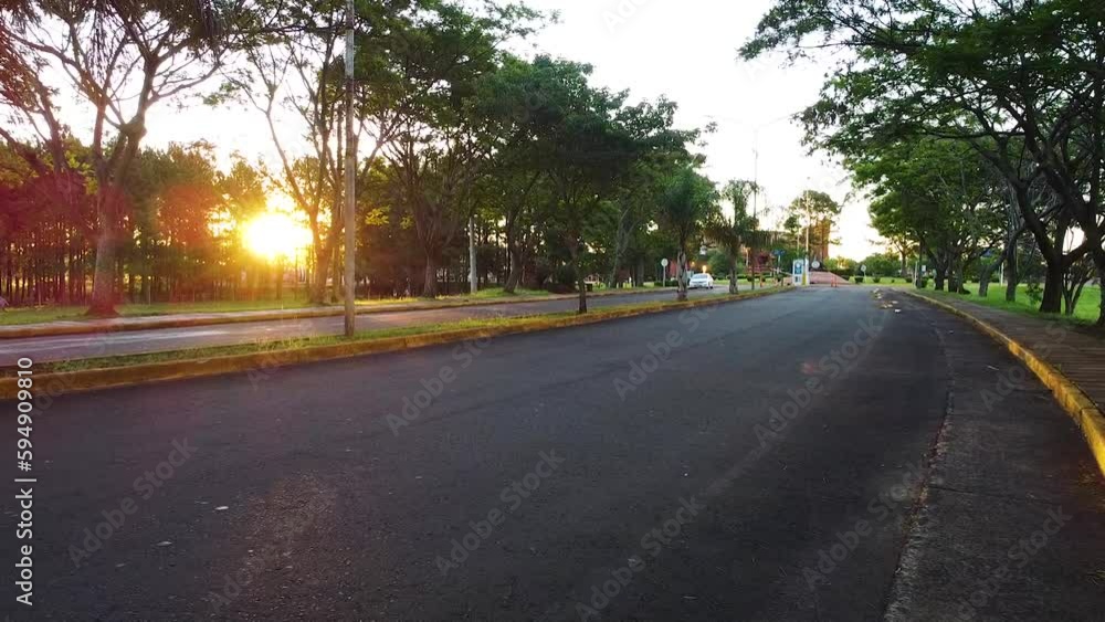Drone clip moving forwards over a dual carriage road, with a peaceful orange sunset visible through the treelined edge Drone clip moving forwards over a dual carriage road, with a peaceful orange sunset visible through the treelined edge
