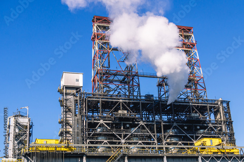 Smoke emissions into the atmosphere. Technological equipment at a chemical plant. White smoke escapes into the atmosphere from the production equipment. White smoke and blue sky. Atmospheric pollution