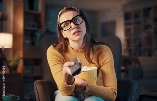 Expressive woman watching television and holding the remote control