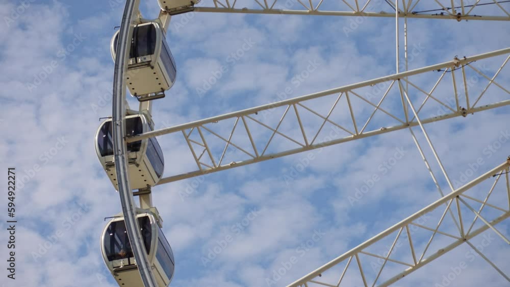 Ferris wheel rotates against background of blue cloudy sky. Amusement park attraction. Summer holidays Ferris wheel rotates against background of blue cloudy sky. Amusement park attraction. Summer holidays