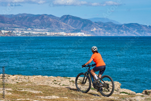 nice senior woman cycling with her electric mountain bike at the Costa Blanca coastline near Nerja, Andalusia, Spain
